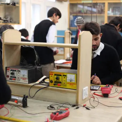 Students conducting a hands-on electricity experiment in a laboratory using electrical test equipment, multimeters, wires and measurement instruments.
