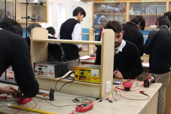 Students conducting a hands-on electricity experiment in a laboratory using electrical test equipment, multimeters, wires and measurement instruments.